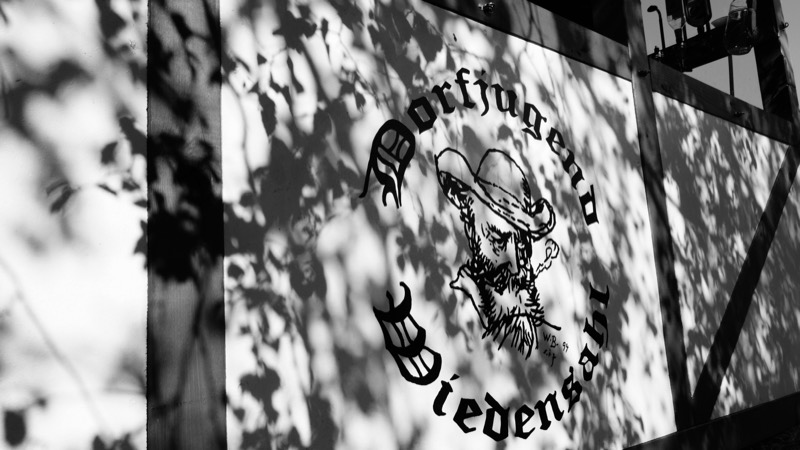 Das Wappen der Dorfjugend auf einem Erntewagen, im Schatten der Blätter